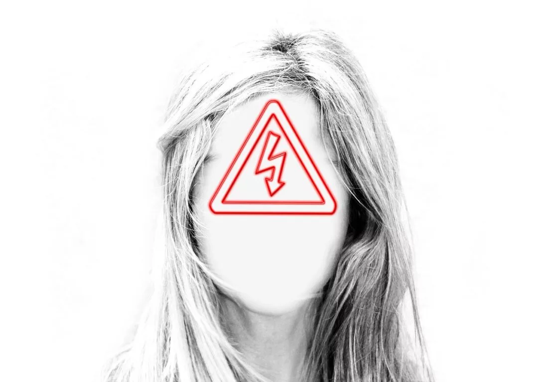 Black-and-white portrait of a woman whose face is covered by a red high-voltage warning sign